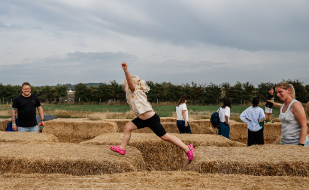 little girl leaping on straw bales